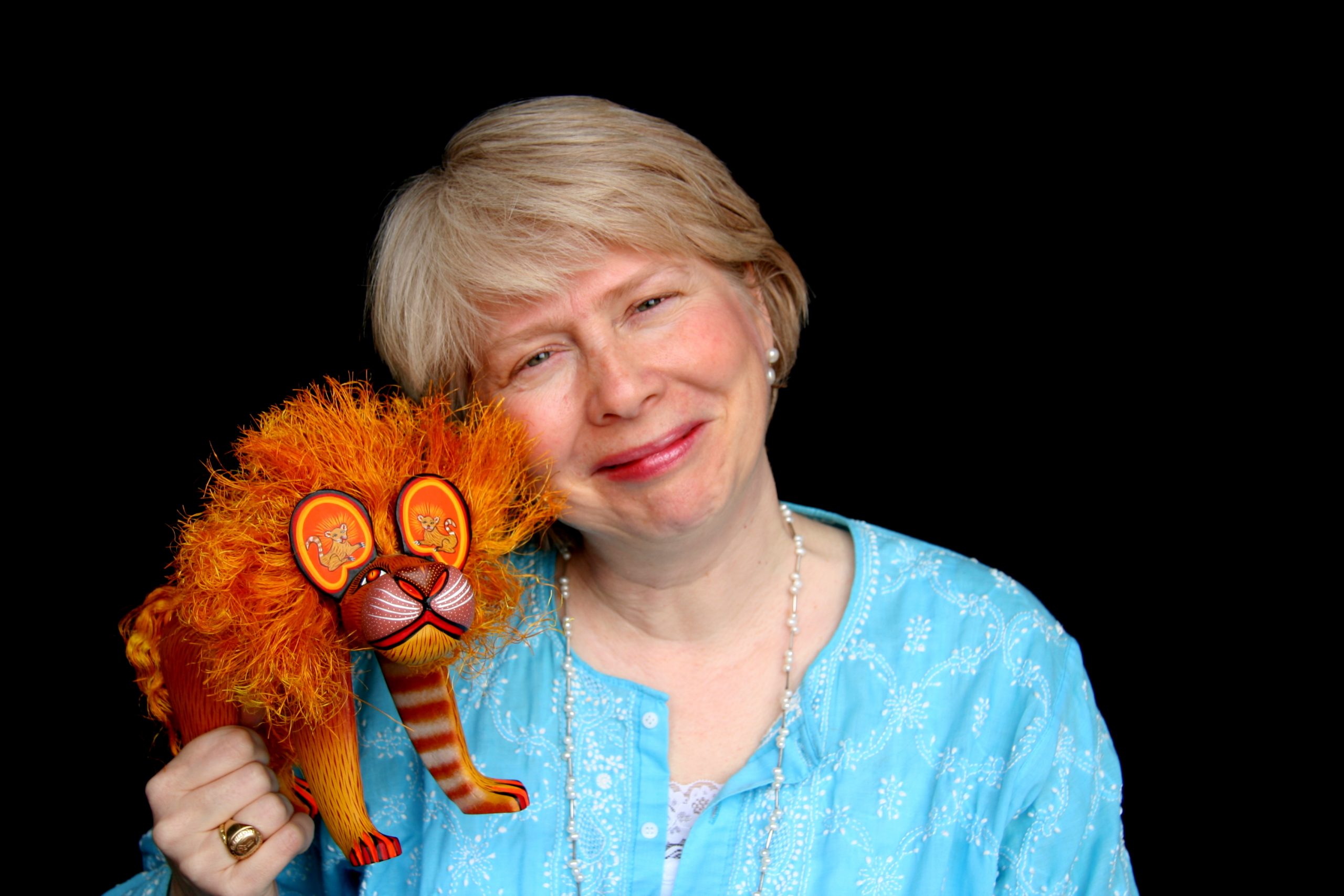 Photo of author Cynthia Weill smiling with a wooden carving of a lion in her right hand.