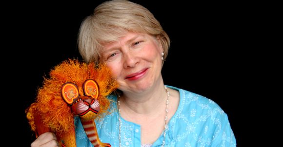 Author Cynthia Weill smiles at the camera while holding a sculpture of a lion.