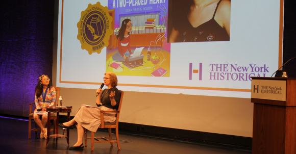 Author Doan Phuong Nguyen and DiMenna Children's History Museum Vice President & Director Alice Stevenson  sit on a stage in conversation about Doan Phuong's NY Historical Children's Book Prize winning title, A Two-Placed Heart.